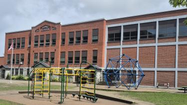 A rectangular brick school building with a playground in front.