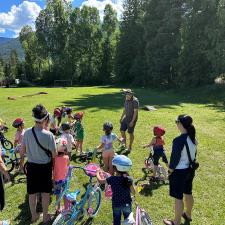 Children and adults stand with their bikes on a grassy field