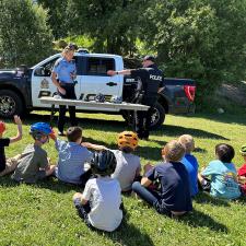 Children sit on the grass in front of police officers